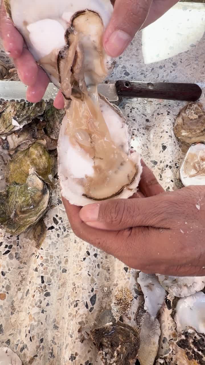 Man carefully opens fresh oyster with knife on textured surface