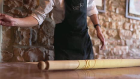 hero shot of an italian chef throwing flour on a wood table to an handmade piece of pasta with a stone wall background