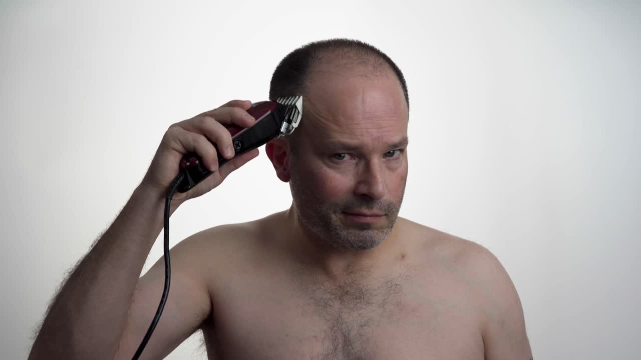 Man facing camera while he uses clippers to cut his own hair