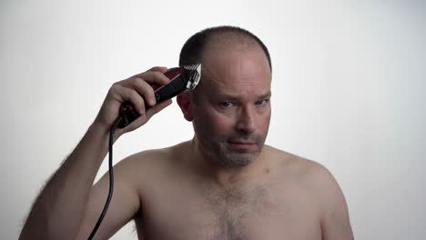 man facing camera while he uses clippers to cut his own hair