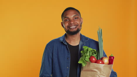 retrato de un tipo alegre satisfecho con comestibles de cultivo casero en una bolsa de papel