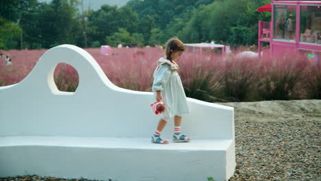 little girl with doll runs on bench outdoors and jumps from it in slow motion - herb island park