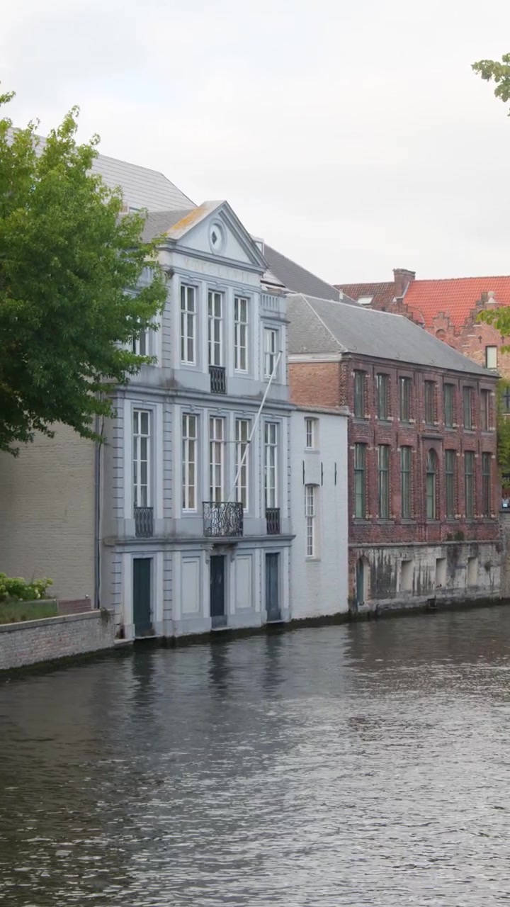 La telecamera panoramica lentamente lungo il tranquillo canale di Bruges, rivelando l'architettura storica lungo il fiume e il fogliame autunnale