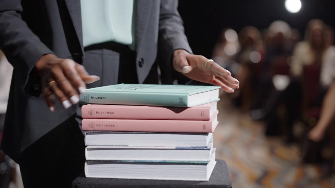 Showcasing a Collection of Business Books During a Professional Event with an Engaged Audience in the Background, Highlighting Education and Networking Opportunities