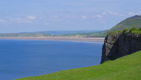 view of rhossili bay from cliff top showing length of the bay along gower coast. beautiful clear blue sea in summer months in wales, uk.
