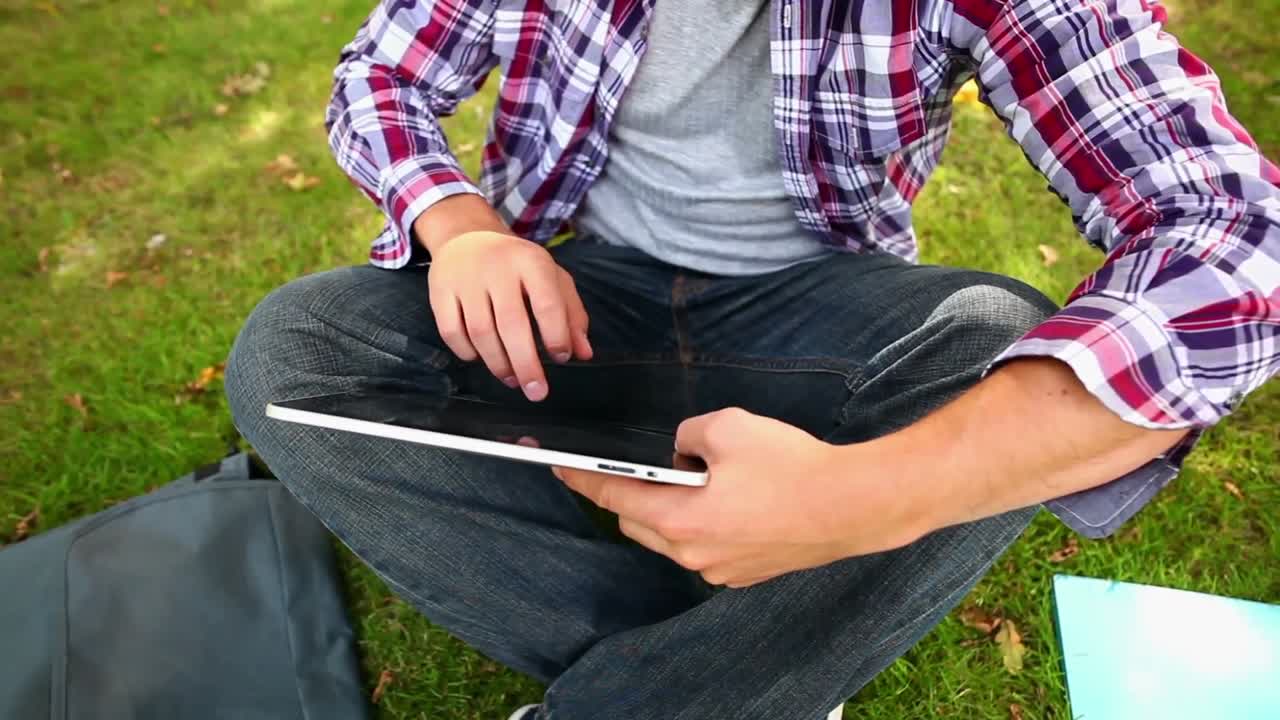 Student sitting on the grass using his tablet