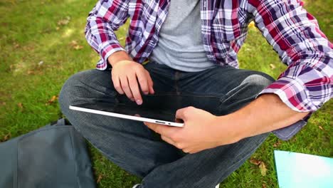 Student-sitting-on-the-grass-using-his-tablet