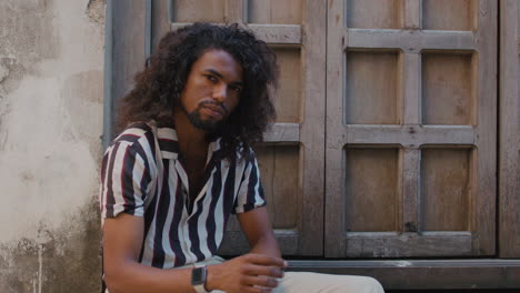 mysteriously looking arabic black man sits under a giant wooden door of an old house