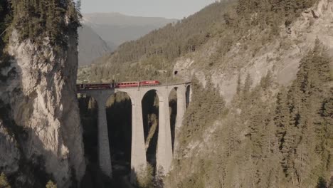 train cross landwasser viaduct tunnels between mountains covered by forests, summer season, aerial dolly in