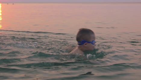 boy in goggles learning to swim with his mother