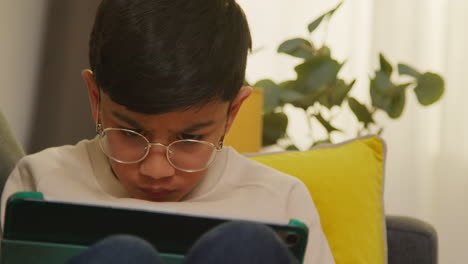 close up of young boy sitting on sofa at home playing games or streaming onto digital tablet 3