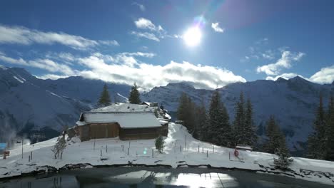 Drone-zooming-in-to-a-cabin-on-the-mountain,-and-slightly-tilting-to-the-snowy-slopes-for-skiing-below,-at-Engelberg,-located-in-Brunni,-Switzerland