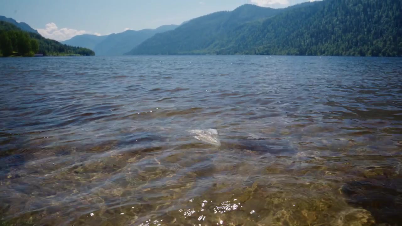 Plastpose flytende i klart innsjøvann med fjellbakgrunn