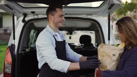 la cliente está recibiendo una bolsa de papel de comestibles orgánicos de un mensajero masculino amigable y sonriente