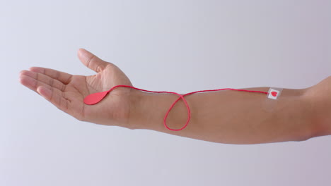 hand of biracial man with blood drop, red string and heart sticking plaster on white, slow motion