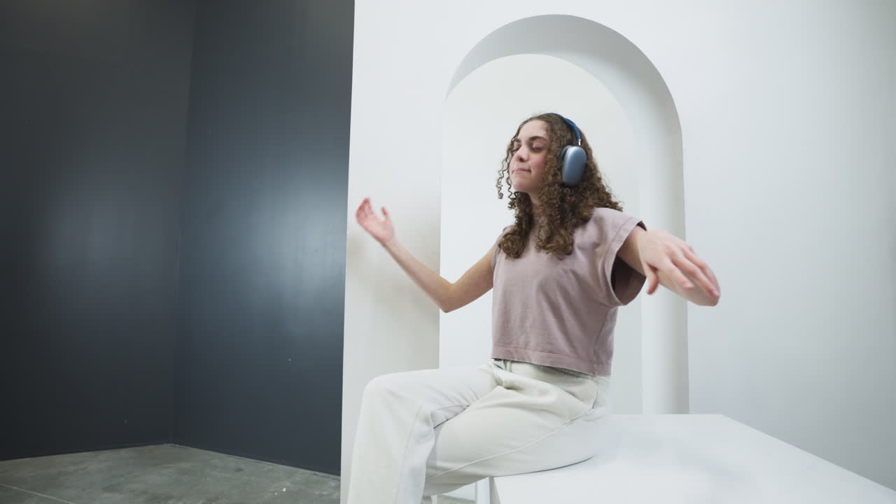 Trendy girl with curly hair dancing effusively while listening to music