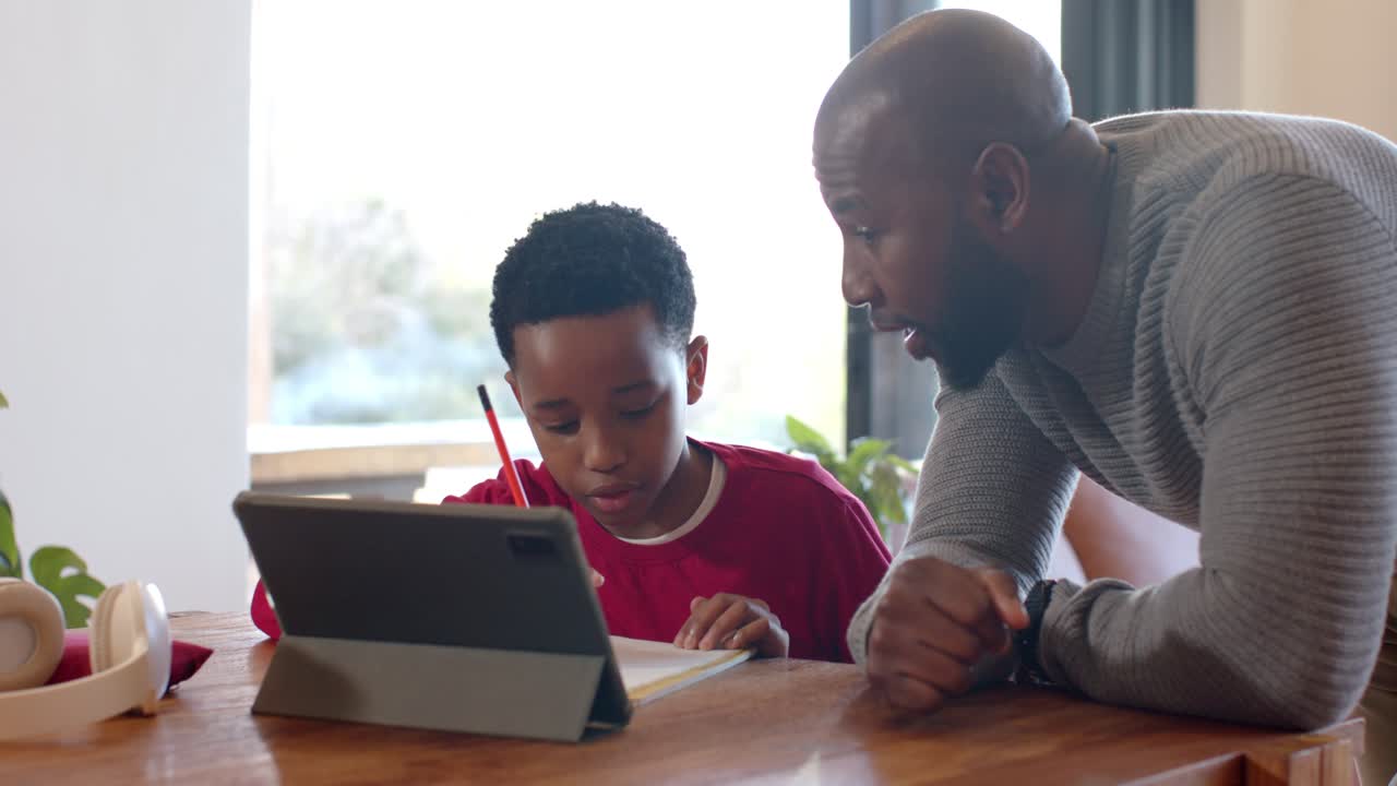African American father and son doing homework after father pointing at tablet prompt at table