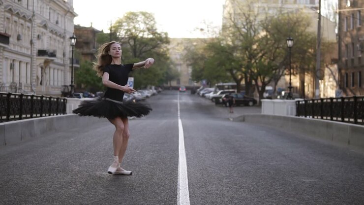 Dancing ballerina in black ballet tutu and black T shirt practicing right on the street. Morning city. Jumping cross the road. Slow motion