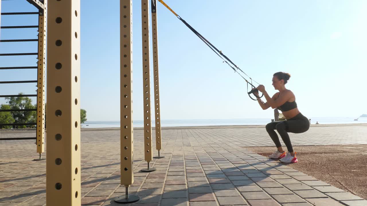 야외 운동. 서스펜션 스트. 스트으로 운동. 운동하는 젊은 여성은 줄을 사용하여 전신 저항 운동을 하고 있습니다. 해가 지거나 해가 뜨는 동안 해변에서. 건강한 생활 방식 개념. 아침 스포츠.