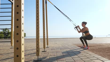 entrenamiento al aire libre. correas de suspensión. entrenamiento con correas. mujer joven atlética está haciendo ejercicios de resistencia de todo el cuerpo usando cuerdas en bucle trx, en la playa durante la puesta o el amanecer. entrenamiento de fitness al aire abierto. concepto de estilo de vida saludable. deporte matutino