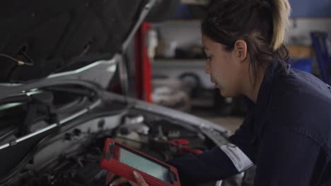 mecánica usando una tableta digital e inspeccionando el automóvil en una estación de servicio de automóviles