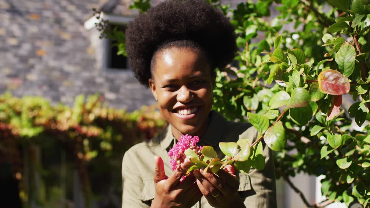 retrato de una mujer afroamericana sonriente de pie en un jardín soleado sosteniendo una planta