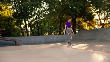 a young girl with a short haircut in a purple top and striped pants rides on roller skates in a skate park on a concrete surface