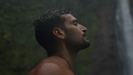 Man with a beard, eyes closed, and his face turned upwards, as rain falls on him. The setting is the lush, green environment of Catarata del Toro, an authentic moment of connection with nature
