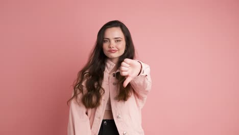 sad young woman showing thumb down in pink studio