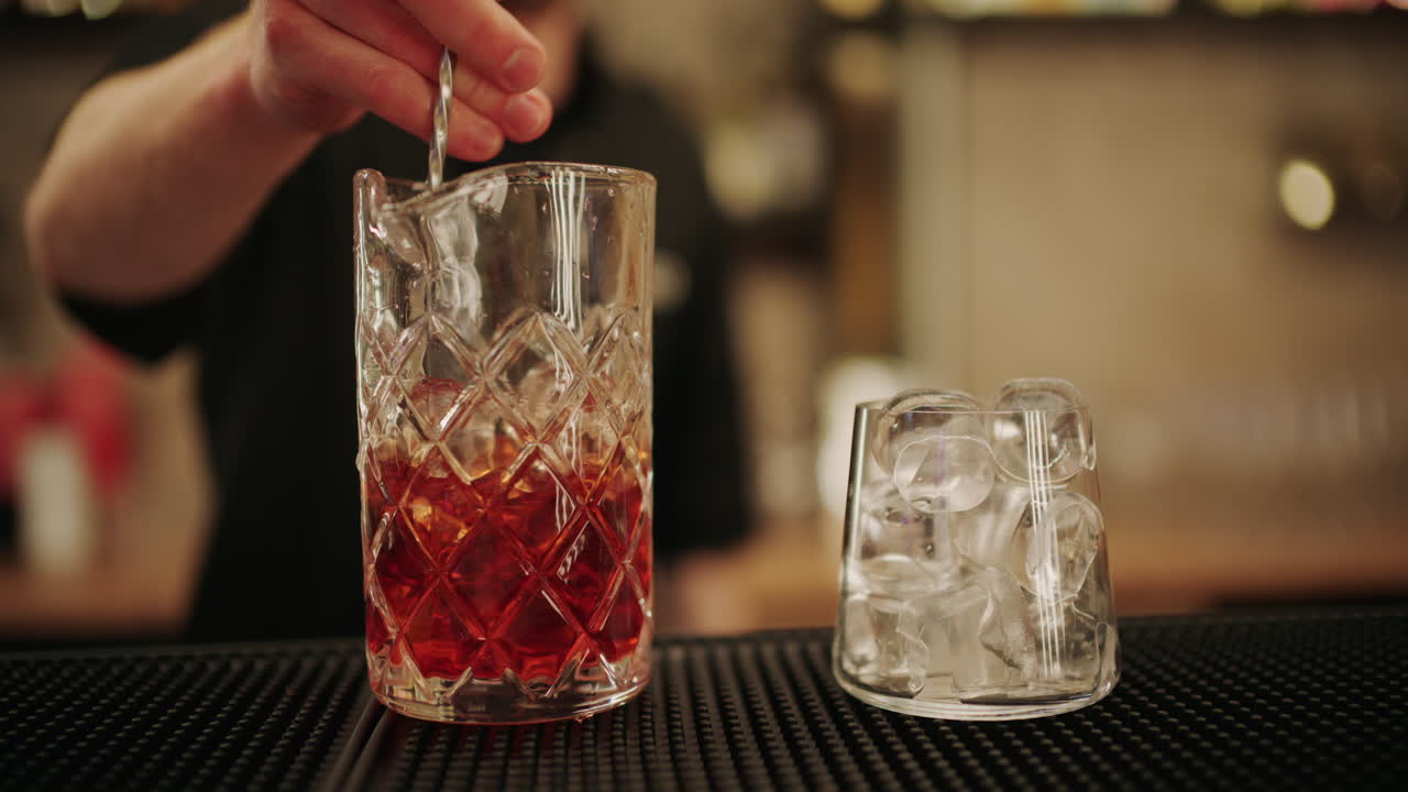 Primo piano di un barman che mescola un cocktail con ghiaccio in un mixing glass di cristallo