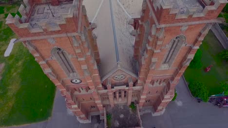 a beautiful old church top close up aerial view, red building of the church, green trees and grass around the church, cross at the top and bottom of the church