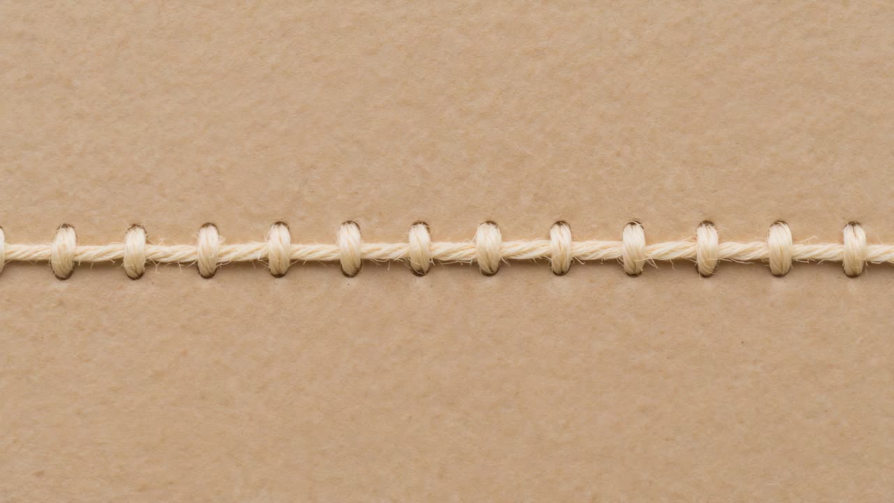 Camera zooming on stitched cream cord to reveal beige paper texture and punched hole edges closeup
