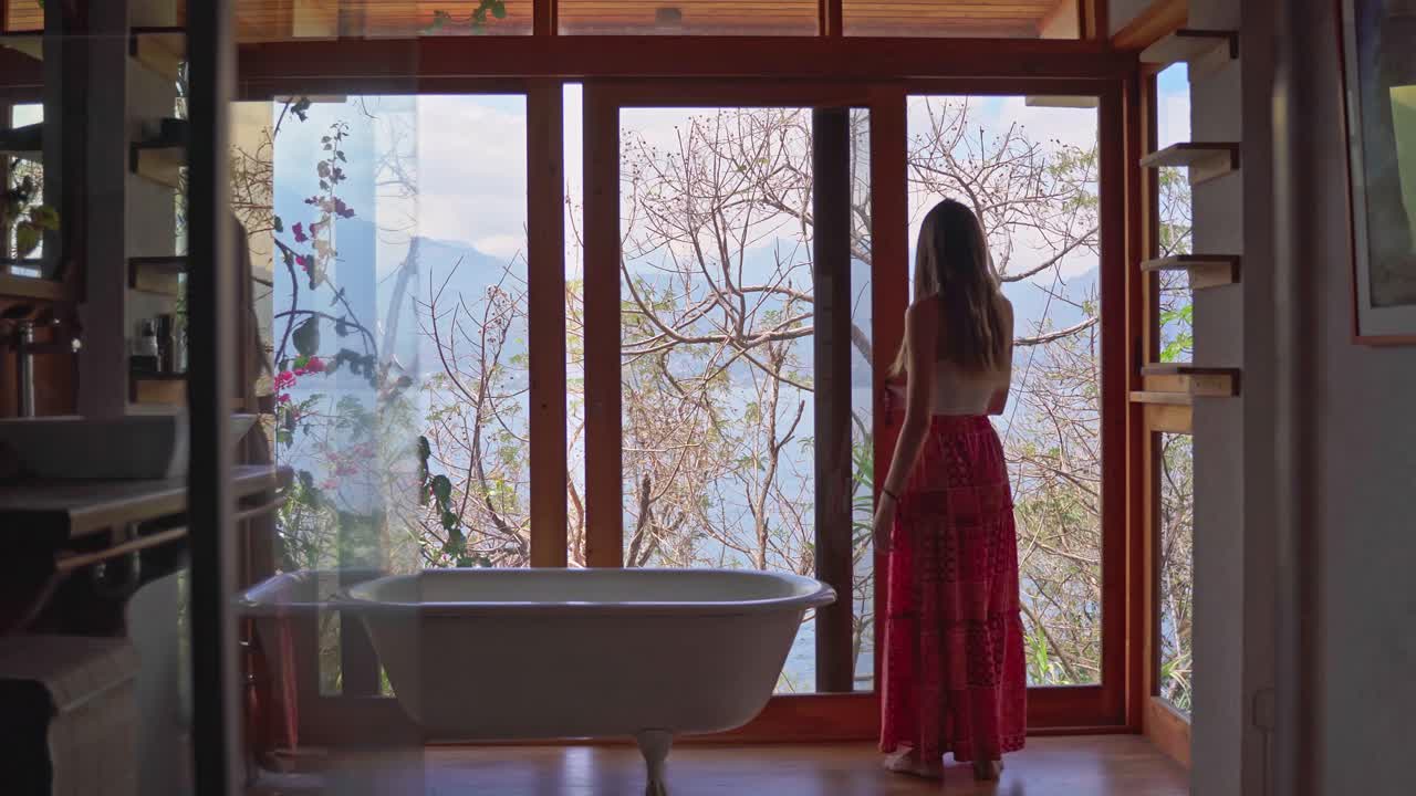 휴가 중인 소녀가 화장실에 들어가서 창문을 열고 과테말라의 아란 호수와 화산의 전망을 볼 수 있습니다.