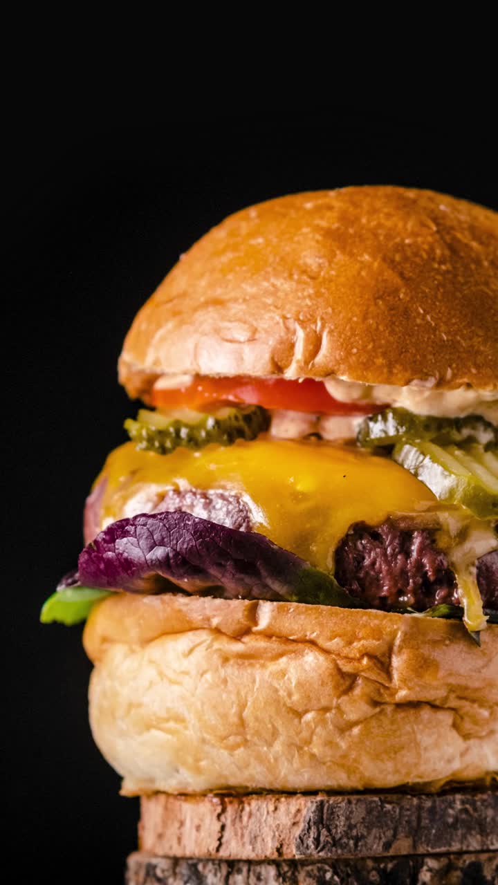 Appetizing burger with freshly baked buns fried patty under cheese and mayonnaise rotating fast on wooden stand against black background. Vertical orientation