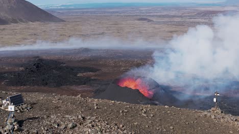 Solar-powered-research-equipment-on-mountain-ridge-with-view-of-exploding-volcano