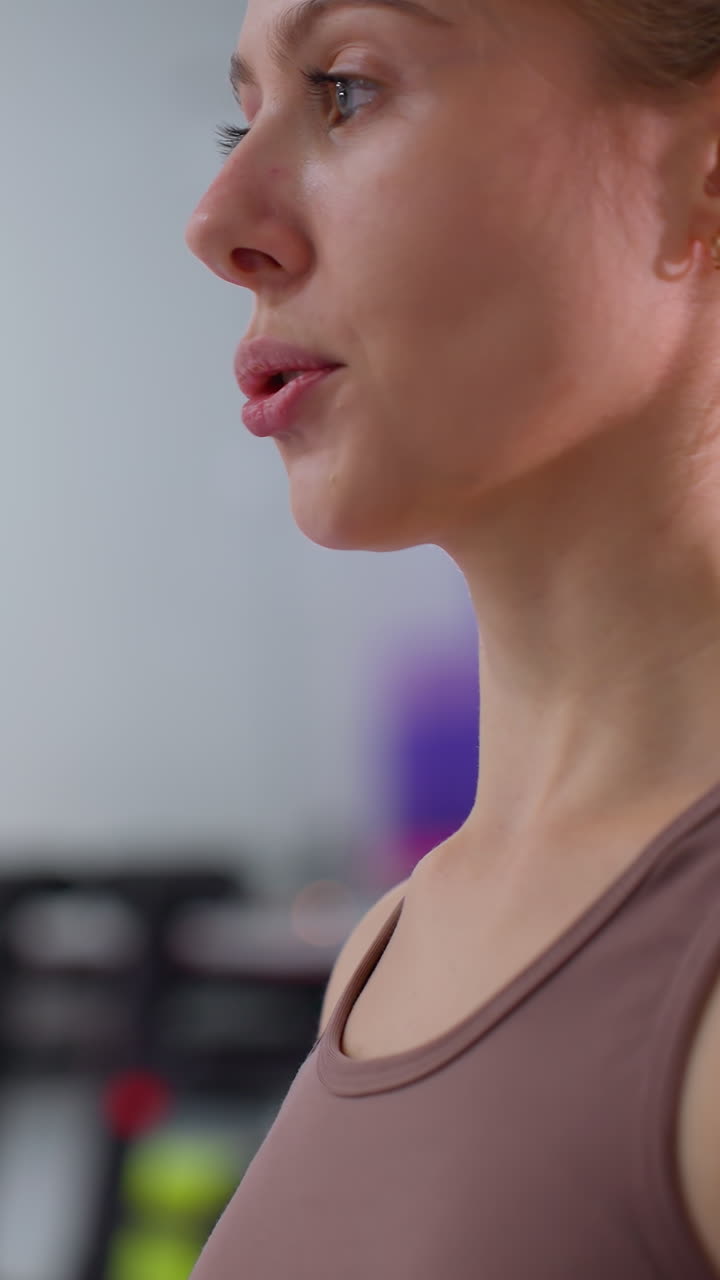 Primo piano di donne sedute su tappetini che eseguono esercizi di stretching delle costole in una palestra ben attrezzata, lo sfondo presenta attrezzature per l'allenamento sfocate, specchi e un ambiente fitness moderno