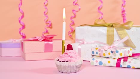 tiempo lapso detener el movimiento de la vela de cumpleaños ardiente en dulce pastel de taza con crema rosada y regalos y cintas detrás