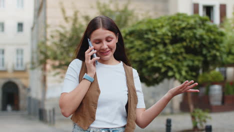 happy young caucasian woman in casual talking gossip on smartphone while walking on city street