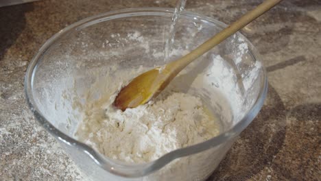 pouring water and olive oil into a bowl of flour