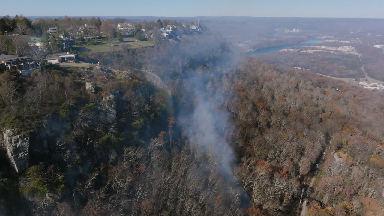 낮에는 산불의 연기를 중심으로 회전하는 공중 영상과 위의 절벽에 소방팀이 있습니다.