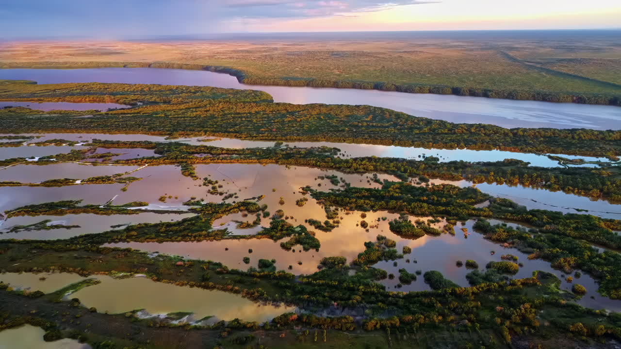 Aerial drone view of vast coastal wetlands with winding water channels and marshland vegetation reflecting sunset light in the Yucatan Peninsula, Mexico