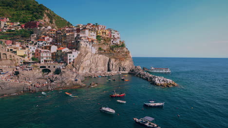 Cinque-Terre-with-the-villages-Monterosso,-Vernazza,-Corniglia,-Manarola-and-Riomaggiore-at-the-Mediterranean-seaside-coast-of-Italy-with-fishing-boat-and-tourists-swimming