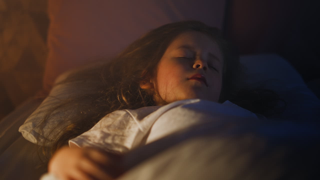 Little girl sleeps with partially illuminated face on bed