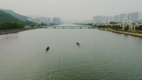 drone approaching a bridge over a river with boats rowing over the water