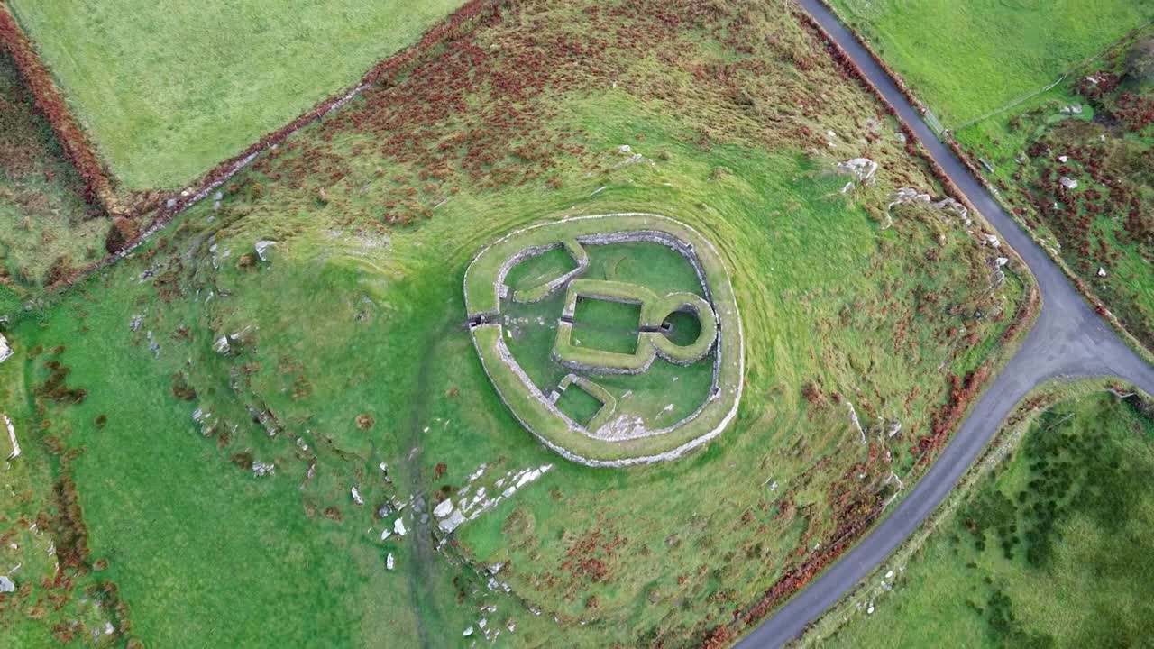 Pemandangan udara dari atas yang menangkap fondasi geometris Leacanabuaile Ringfort kuno, terawat indah di tengah hijaunya pepohonan rimbun pedesaan Kerry, Irlandia