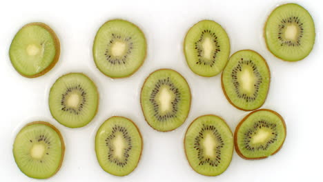 sur un fond blanc, des kiwis tranchés sont aspergés d'eau. l'eau tombe sur des kiwis juteux.