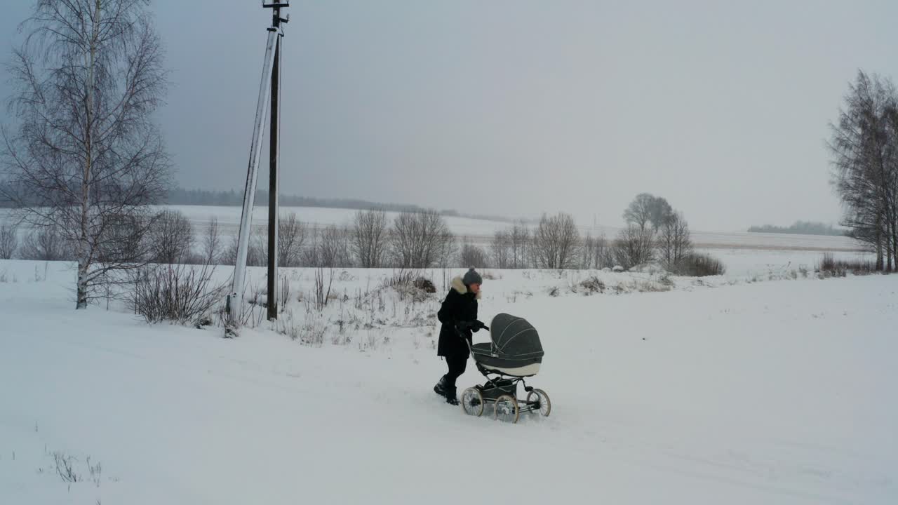 검은색 재을 입은 여성이 눈 인 도로에서 아기 트롤러와 함께 고, 겨울