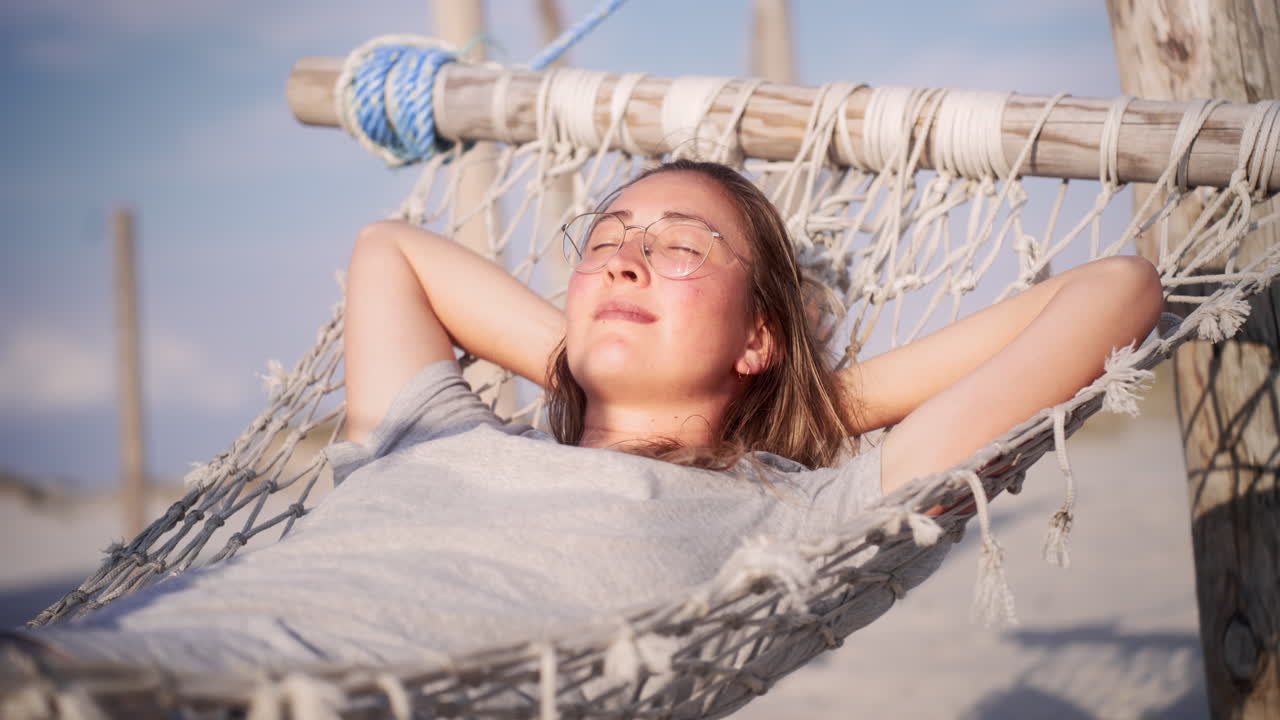 mujer joven relajándose en una hamaca en la playa, sonriendo
