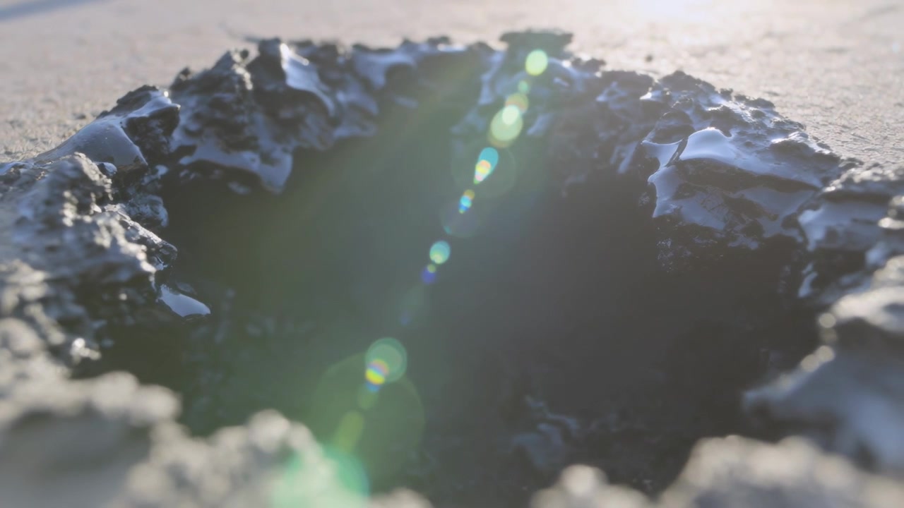 Casting strong backlight, sun creating green flare and revealing crusty crater rim on sandy plain