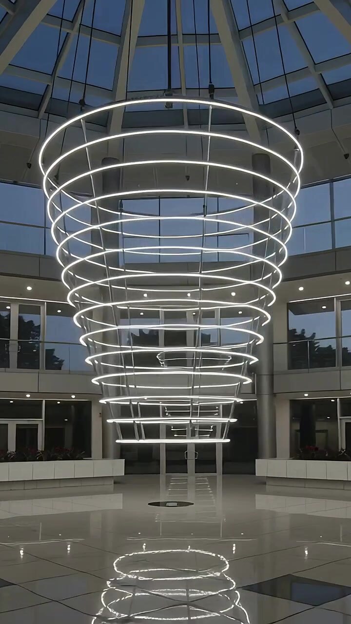 Video vertical: Espiral LED suspendida que pulsa al atardecer bajo una cúpula, con reflejo cambiante en el suelo